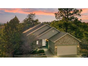 Charming home with a stone garage, well-manicured landscaping, and colorful sunset skies at 7649 Pineridge Ter, Castle Pines, CO 80108