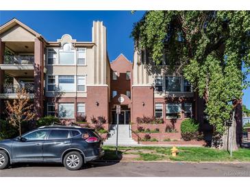 Attractive condominium building with red brick and tan facade, a car parked in front and greenery around the building at 1735 N Ogden St # 106, Denver, CO 80218