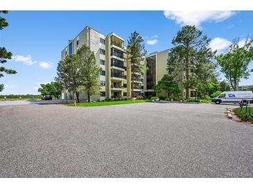View of the building featuring an asphalt parking lot, exterior landscaping, and an array of green trees at 13902 E Marina Dr # 303, Aurora, CO 80014