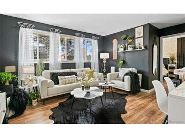 Inviting living room featuring dark walls, wood floors, and bright natural light from the large windows at 10211 Ura Ln # 10-105, Thornton, CO 80260