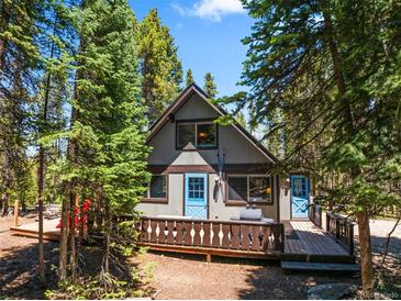 Charming cabin exterior with blue doors, a spacious deck, and surrounded by tall, mature trees at 91 Slalom Dr, Breckenridge, CO 80424