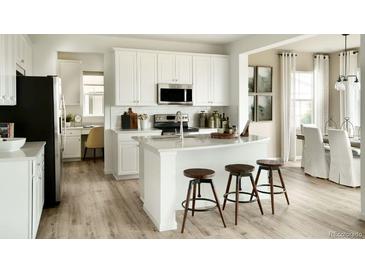 Modern kitchen featuring white cabinetry, stainless steel appliances, an island with stools, and hardwood flooring at 39733 Penn Rd, Elizabeth, CO 80107