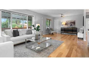 Bright living room featuring hardwood floors, a modern glass coffee table, and large windows overlooking the backyard at 3222 S Fairfax St, Denver, CO 80222