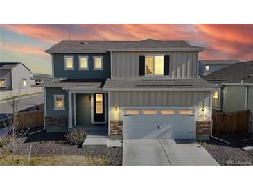 Charming two-story home featuring mixed siding, stone accents, an attached two-car garage, and beautiful sunset sky at 17947 E 95Th Ave, Commerce City, CO 80022