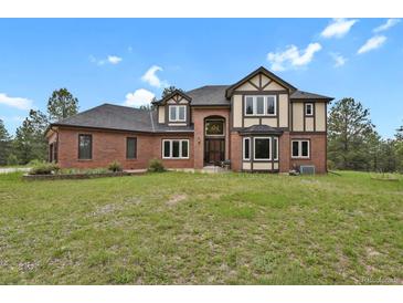 Stately brick and Tudor-style home with a manicured lawn and mature trees at 1972 Gold Camp Way, Franktown, CO 80116