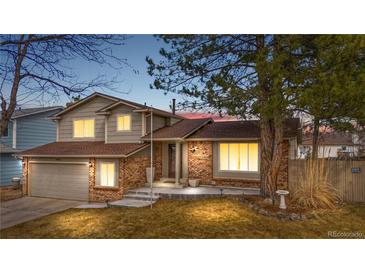 Charming two-story home with brick accents, lush lawn, mature trees, and warm exterior lighting at dusk at 3930 S Argonne Way, Aurora, CO 80013