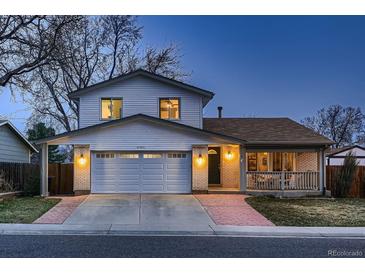 Charming home featuring an attached two-car garage, covered front porch, and well-maintained landscaping at dusk at 8485 W 74Th Dr, Arvada, CO 80005