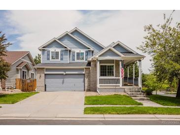 Charming two-story home featuring a covered porch, gray siding and a two car attached garage and landscaped front yard at 15389 E 99Th Way, Commerce City, CO 80022