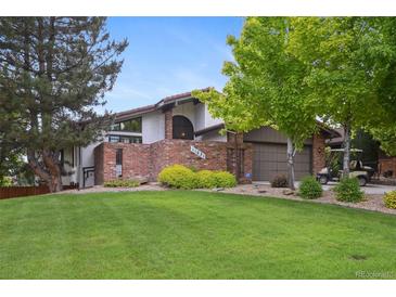 Charming home featuring a brick facade, lush lawn, and mature trees providing shade and curb appeal at 11621 Shoshone Way, Denver, CO 80234