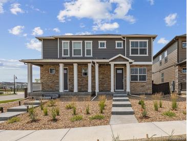 Charming two-story home with stone accents, covered porch, and landscaped front yard with blue sky at 18708 E 99Th Ave, Commerce City, CO 80022
