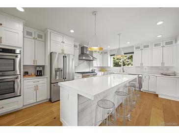Bright, modern kitchen features white cabinetry, stainless steel appliances, and a large center island with seating at 5853 S Havana Ct, Englewood, CO 80111