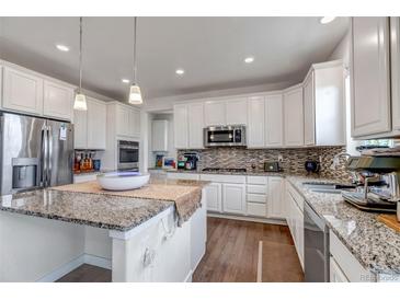 Bright kitchen features stainless steel appliances, granite countertops, island, and a tile backsplash at 8255 S Vandriver Way, Aurora, CO 80016