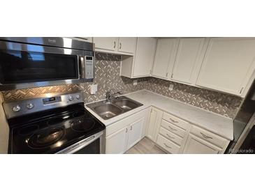 Well-lit kitchen with stainless steel appliances, white cabinetry, and decorative backsplash at 8828 E Florida, Denver, CO 80247