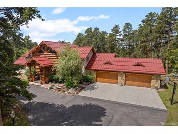 Beautiful log home with red roof and three-car garage nestled in lush greenery at 23076 Oehlmann Park Rd, Conifer, CO 80433