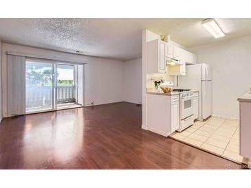 Bright living room featuring hardwood floors, a balcony and open access to a kitchen with white cabinetry at 10762 E Exposition Ave # 336, Aurora, CO 80012