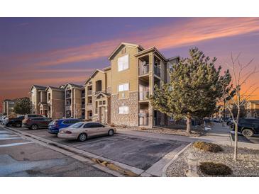 View of the apartments with stone accents, balconies, and ample parking space at dusk at 17525 Wilde Ave # 307, Parker, CO 80134