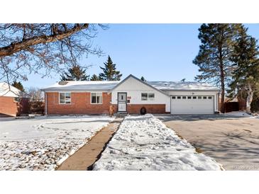 Brick ranch home with attached garage, snowy yard, and walkway at 420 Racine St, Aurora, CO 80011