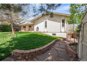 Beautifully landscaped backyard with lush green grass, a stone patio, and mature trees providing shade and privacy at 12662 W Asbury Pl, Lakewood, CO 80228