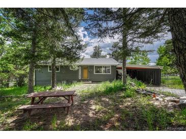Charming exterior of a single-story home with a picnic table sitting under mature trees at 25694 Stansbery St, Conifer, CO 80433