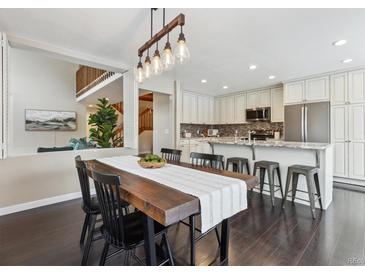 Open-concept dining room adjacent to kitchen, featuring dark wood floors and a modern light fixture at 2067 E Phillips Pl, Centennial, CO 80122
