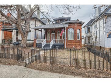 Charming brick home featuring a welcoming front porch and a classic black wrought iron fence at 1229 Josephine St, Denver, CO 80206