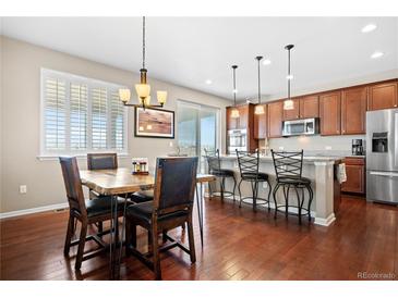 Charming dining area featuring hardwood floors and stylish lighting fixture open to the kitchen and breakfast bar at 16525 Sanford St, Mead, CO 80542