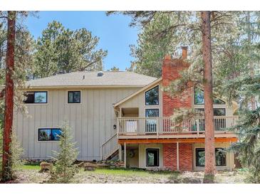 Charming home featuring a red brick chimney and a lovely deck surrounded by lush greenery and mature trees at 8795 Rudd Rd, Evergreen, CO 80439