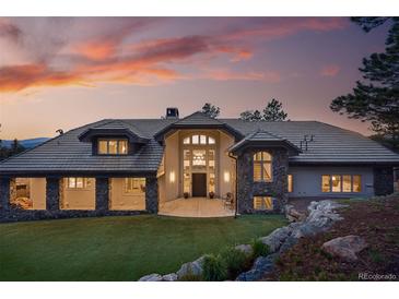 Stunning luxury home with a stone and stucco exterior, tile roof, and lush green lawn at sunset at 2548 Keystone Dr, Evergreen, CO 80439