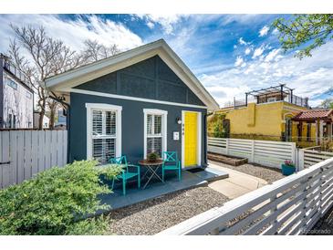 Charming home with a bright yellow door, white fence, and quaint outdoor seating area at 444 Inca St, Denver, CO 80204