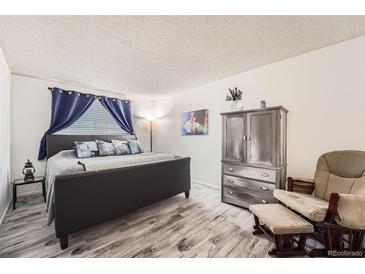 Cozy bedroom featuring a stylish gray bed frame, wood-look flooring and white walls at 7695 E Quincy Ave # 105, Denver, CO 80237