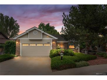 Charming single-story home with a well-maintained lawn, mature trees and two-car garage, bathed in the warm light of dusk at 1181 E 130Th Pl, Thornton, CO 80241