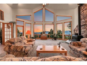 Spacious living room features stunning mountain views from expansive windows and a cozy stone fireplace at 13954 Pine Country Ln, Conifer, CO 80433