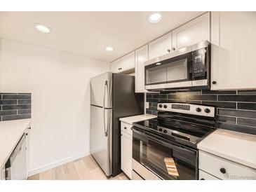 A modern kitchen with stainless steel appliances, sleek black backsplash, and white cabinets at 4691 S Decatur St # 215, Englewood, CO 80110