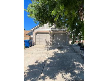 Attached two car garage with brick facade and long concrete driveway partially shaded by a mature tree at 4296 S Halifax Way, Aurora, CO 80013