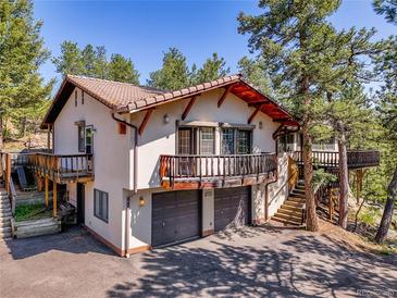 Two-story stucco home with tile roof, balconies, and two-car garage amid mature trees at 5336 High Rd, Evergreen, CO 80439