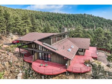 Stunning home with a red wrap-around deck and beautiful mountain views surrounded by evergreen trees at 135 Poorman Rd Rd, Boulder, CO 80302