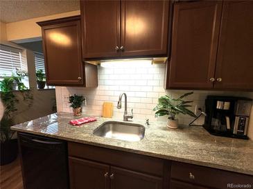 This kitchen features a stainless steel sink, granite counters, tile backsplash, and dark wood cabinets at 10702 E Exposition Ave # 101, Aurora, CO 80012