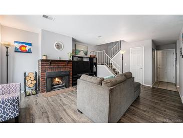 Cozy living room features a brick fireplace, hardwood floors, and staircase with white rails at 2016 W 101St Ave, Thornton, CO 80260