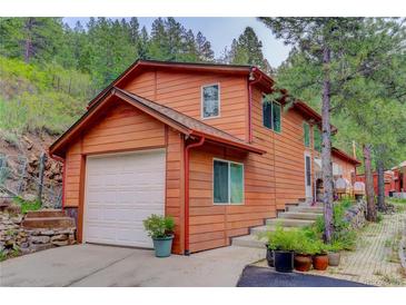 Charming home featuring wood siding, attached garage, and picturesque landscaping at 11220 S Deer Creek Rd, Littleton, CO 80127