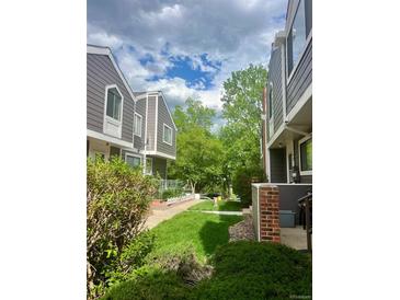 View of gray townhomes with green grass and mature trees, offering a peaceful neighborhood setting at 6836 W 84Th Cir # 15, Arvada, CO 80003