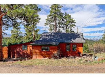 Rustic log cabin with a gray roof, surrounded by trees and with a view of snow-capped mountains in the distance at 6743 Wild Rose Ln, Evergreen, CO 80439