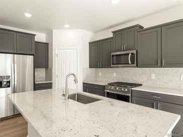 Modern kitchen featuring stainless steel appliances, grey cabinetry, mosaic backsplash, and a spacious island with granite countertop at 6068 Corral St, Brighton, CO 80601