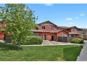 Charming red townhome with lush green lawn, mature tree, and inviting entrance at 1775 Aspen Meadows Cir, Denver, CO 80260