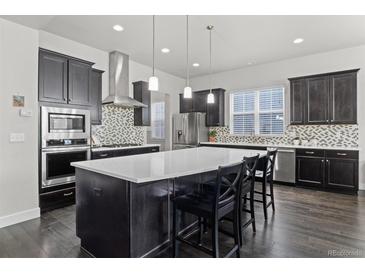 A spacious kitchen with dark cabinets, a mosaic backsplash, stainless steel appliances, and a large center island at 1867 W 137Th Ln, Broomfield, CO 80023
