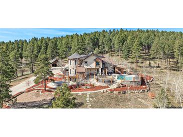 Stunning home with a stone exterior, multiple decks and outdoor entertainment areas, set amidst a lush, wooded landscape at 12555 Critchell Ln, Littleton, CO 80127