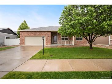 Charming brick home featuring a well-manicured lawn, mature tree, and inviting front porch at 9040 Grand Mesa Ave, Longmont, CO 80504
