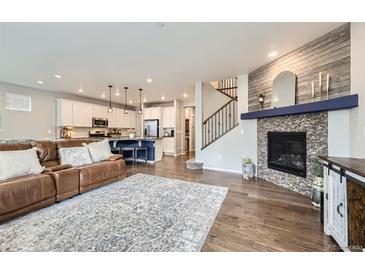 Open-concept living room with a modern fireplace, wood floors, and seamless access to a stylish kitchen at 14147 Hudson St, Thornton, CO 80602