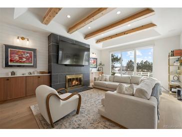 Bright living room featuring a fireplace, wood beams, large windows, and modern furnishings at 7079 S Locust Pl, Centennial, CO 80112