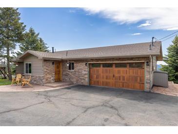 Charming single-story home featuring stone accents, a wooden garage door, and a well-maintained asphalt driveway at 24030 San Isabel Rd, Indian Hills, CO 80454