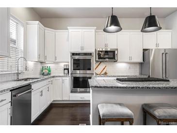 Modern kitchen with white cabinets, stainless steel appliances, granite counters, and island seating at 181 S Monaco Pkwy, Denver, CO 80224